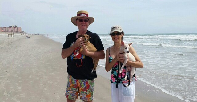 A couple stands on a beach holding their two dogs